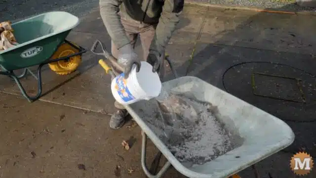 adding water and mixing concrete in a wheelbarrow with a shovel